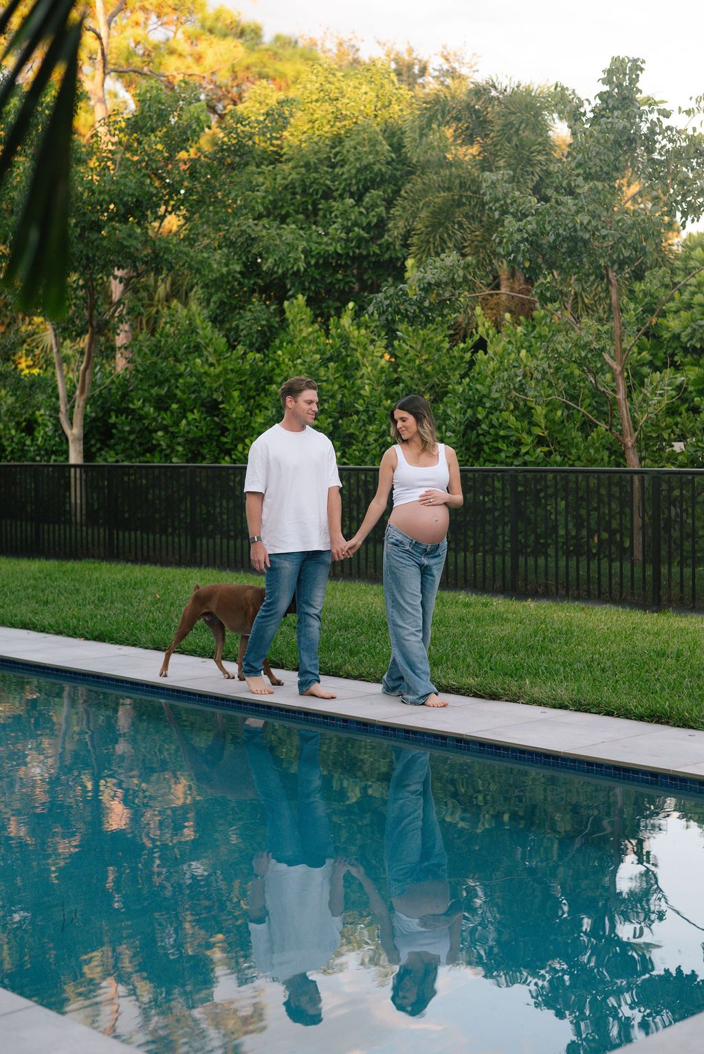 A couple sits together by a blue swimming pool during golden hour.