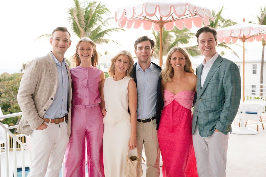 Group photo on tropical balcony with pink umbrellas, wearing coordinated summer formal attire.
