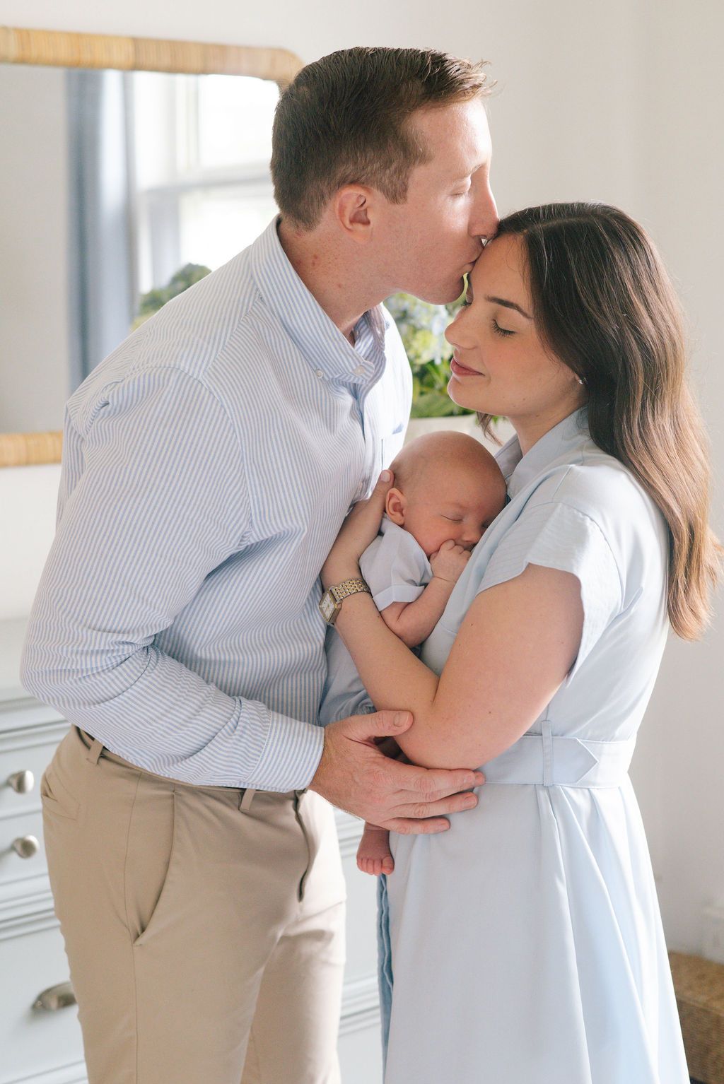 Intimate family moment as parents hold their sleeping newborn in a bright, modern nursery setting.
