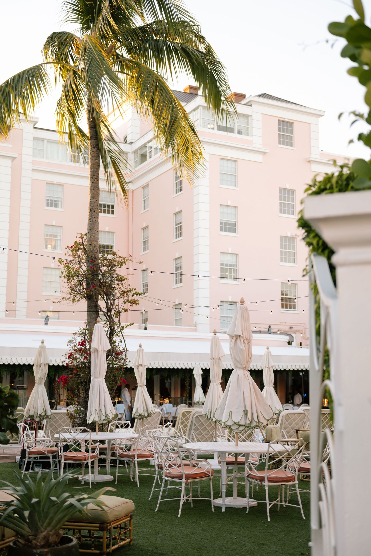 Pink luxury hotel with palm trees and outdoor wedding reception setup on manicured lawn.