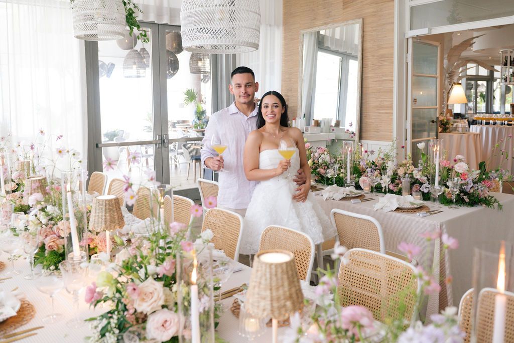 An elegant wedding reception setup with pink and white floral arrangements and rattan chairs.