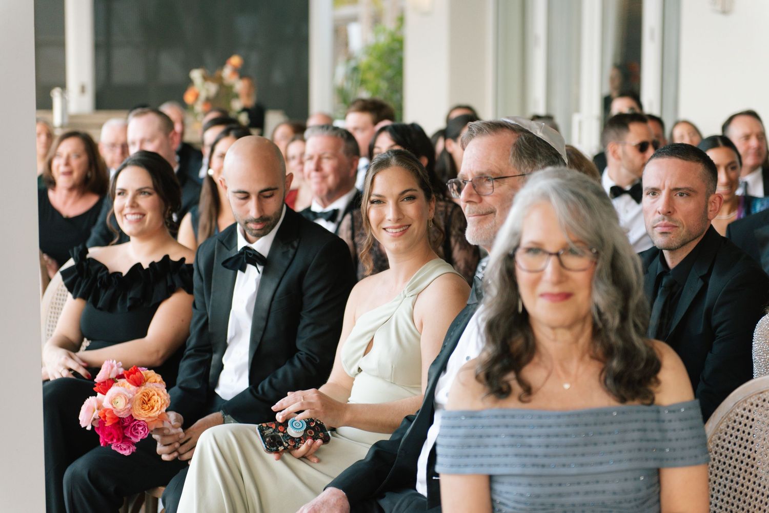 Wedding guests seated in rows watch the ceremony in an elegant indoor venue.