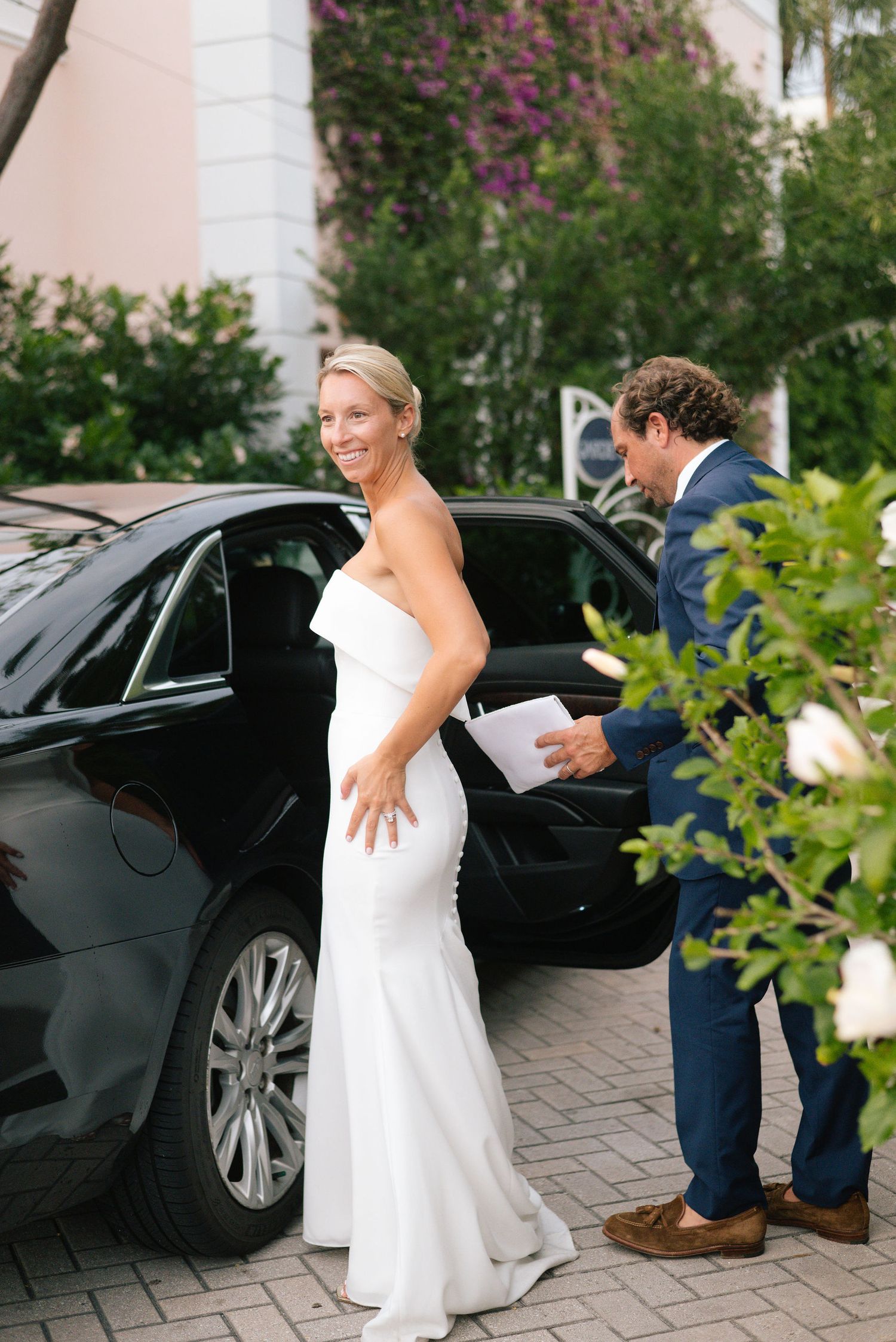 Wedding couple getting into a black luxury car on a brick driveway.