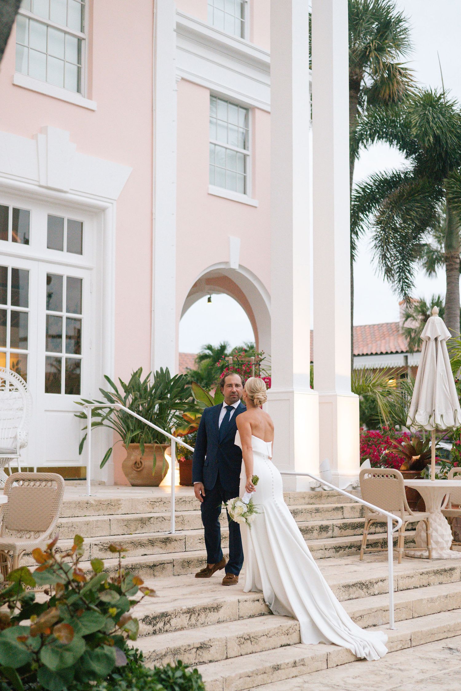 Bride and groom share intimate moments on the grand steps of a pink resort.