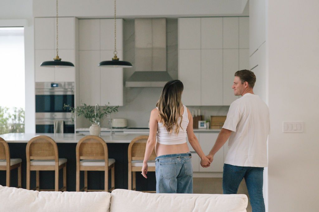Couple in casual attire sharing an intimate moment in a modern white kitchen with wooden bar stools.