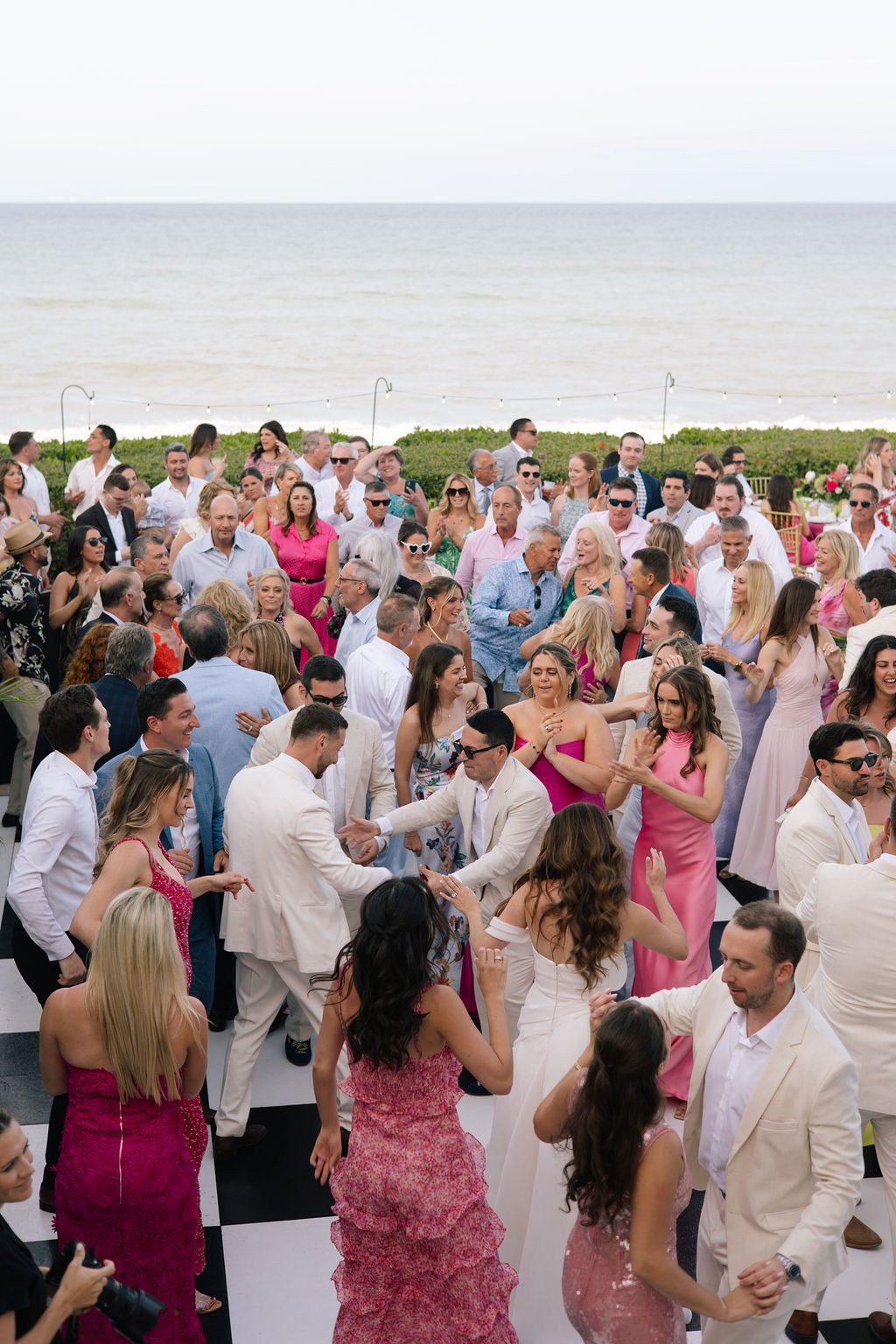 Outdoor wedding reception with guests dancing and mingling in pink and white attire.