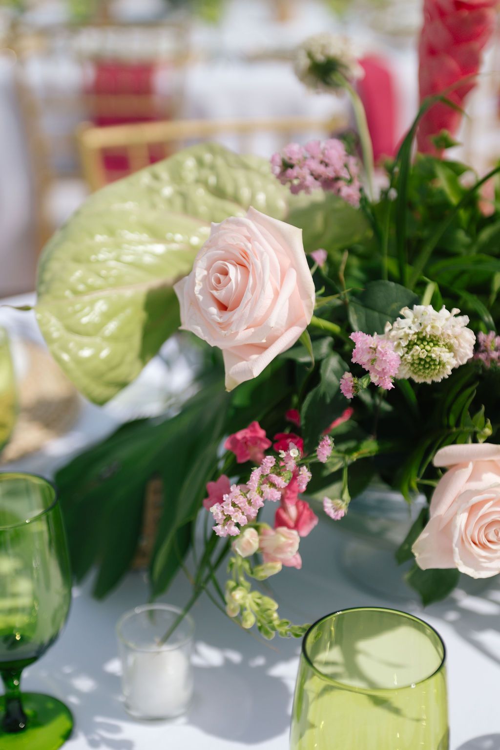 Elegant table decorations featuring pink roses and green foliage in glass vases.