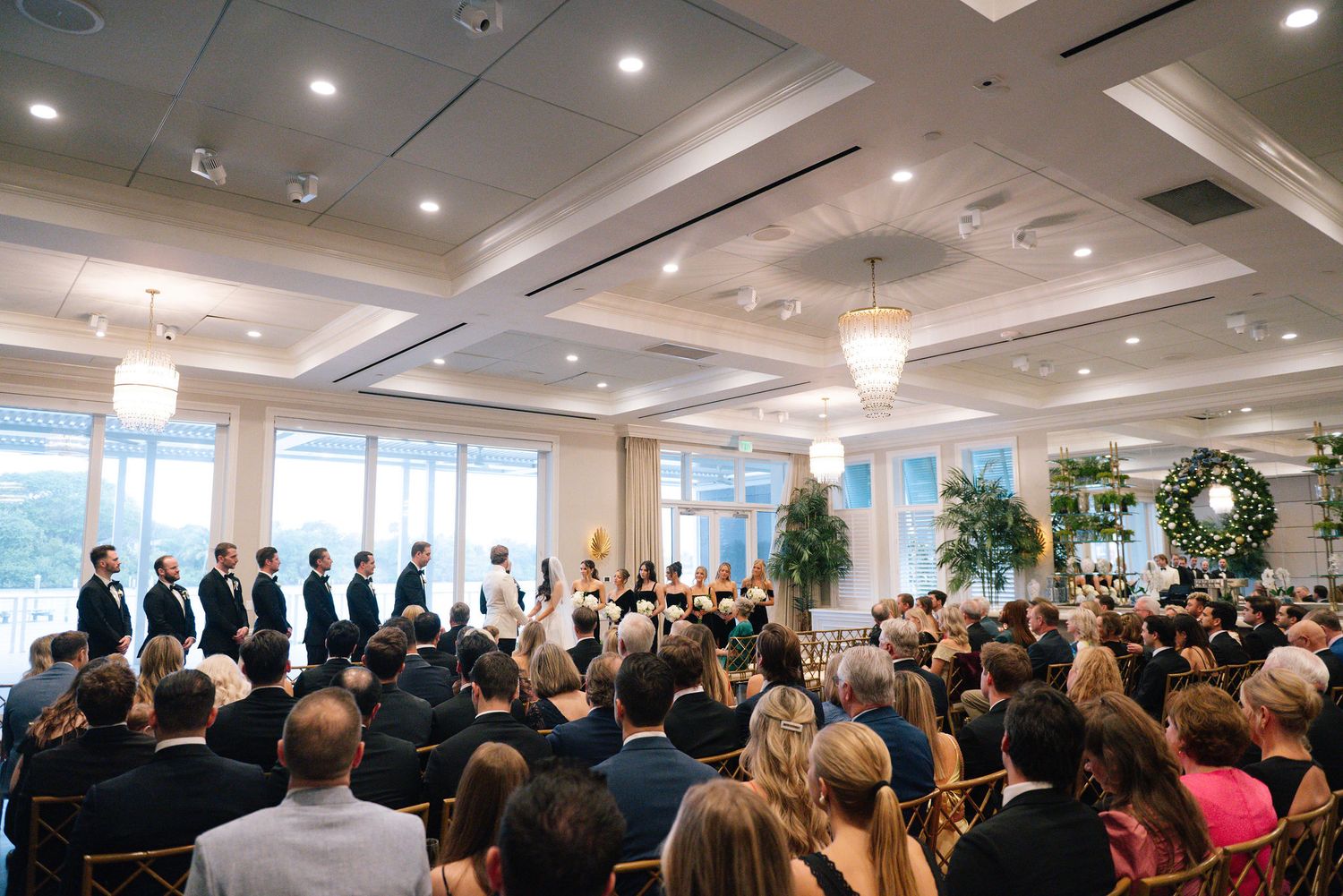 Large crowd of wedding guests seated in rows during indoor ceremony.