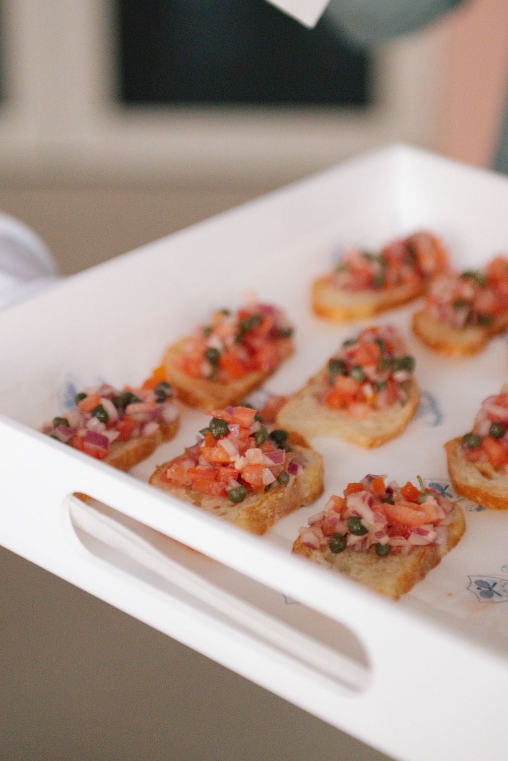 Bruschetta appetizers with tomato topping served on white serving tray.
