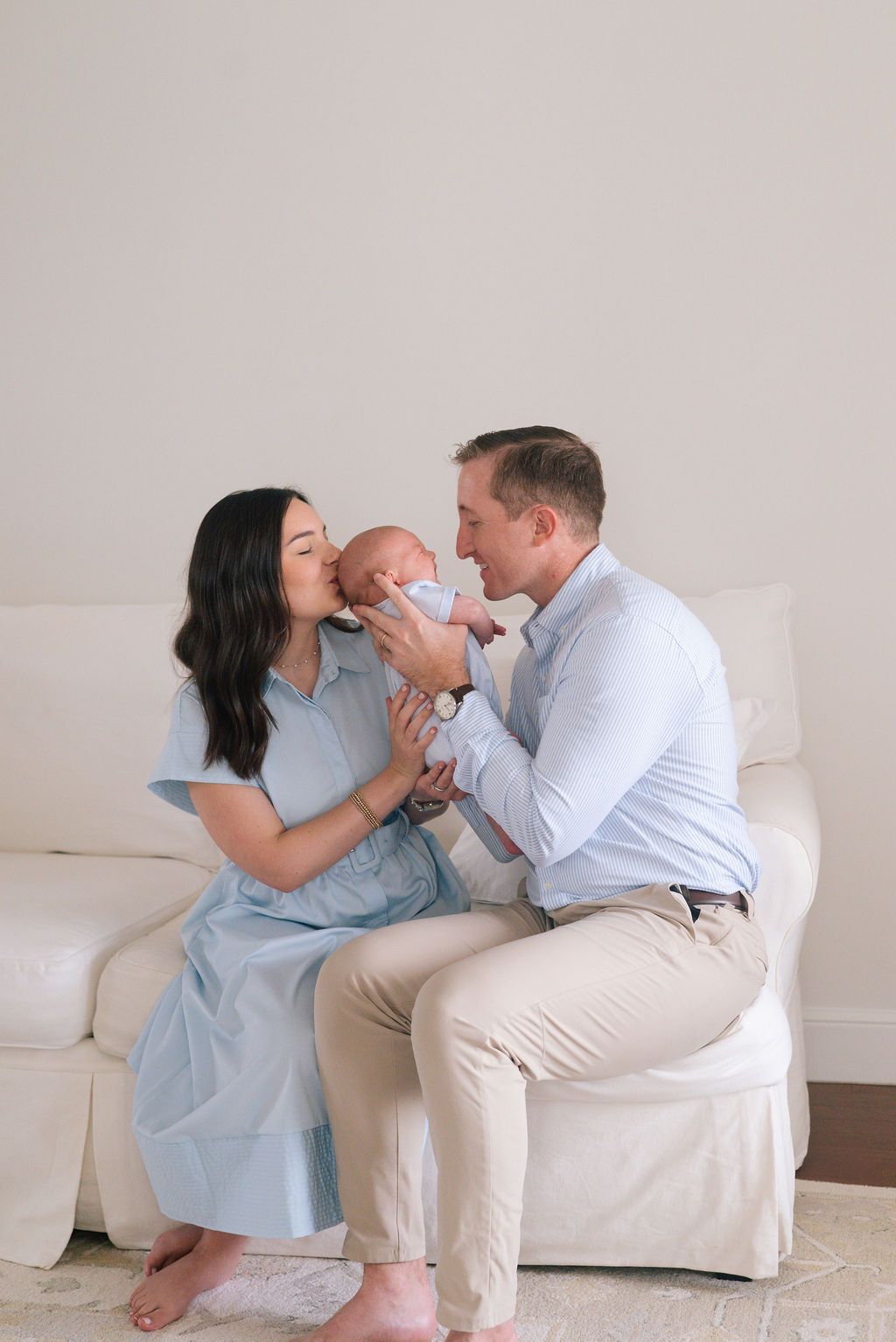 Family sitting on white couch sharing tender moments with their newborn baby.