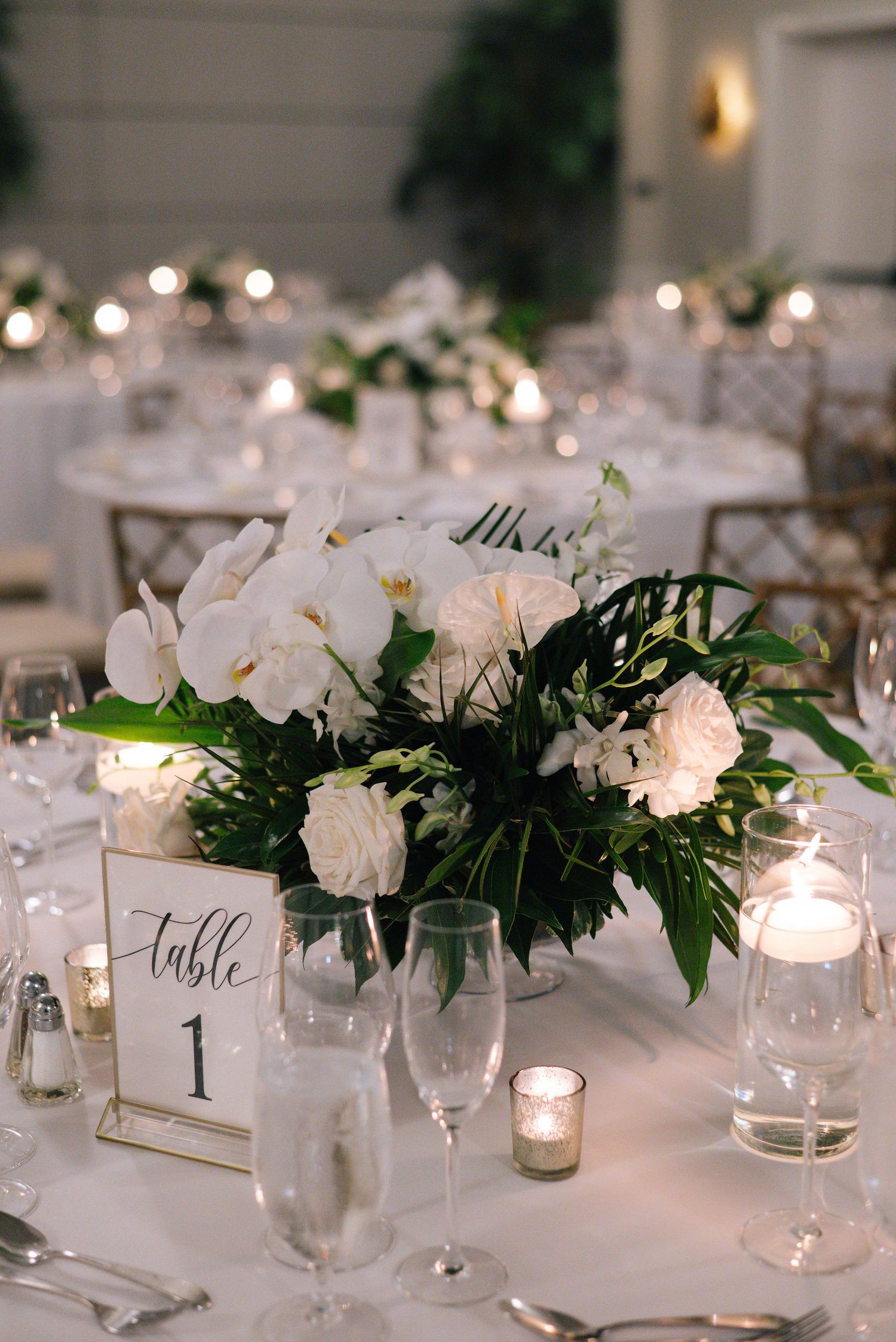 Elegant white floral centerpieces with candles on wedding reception tables.