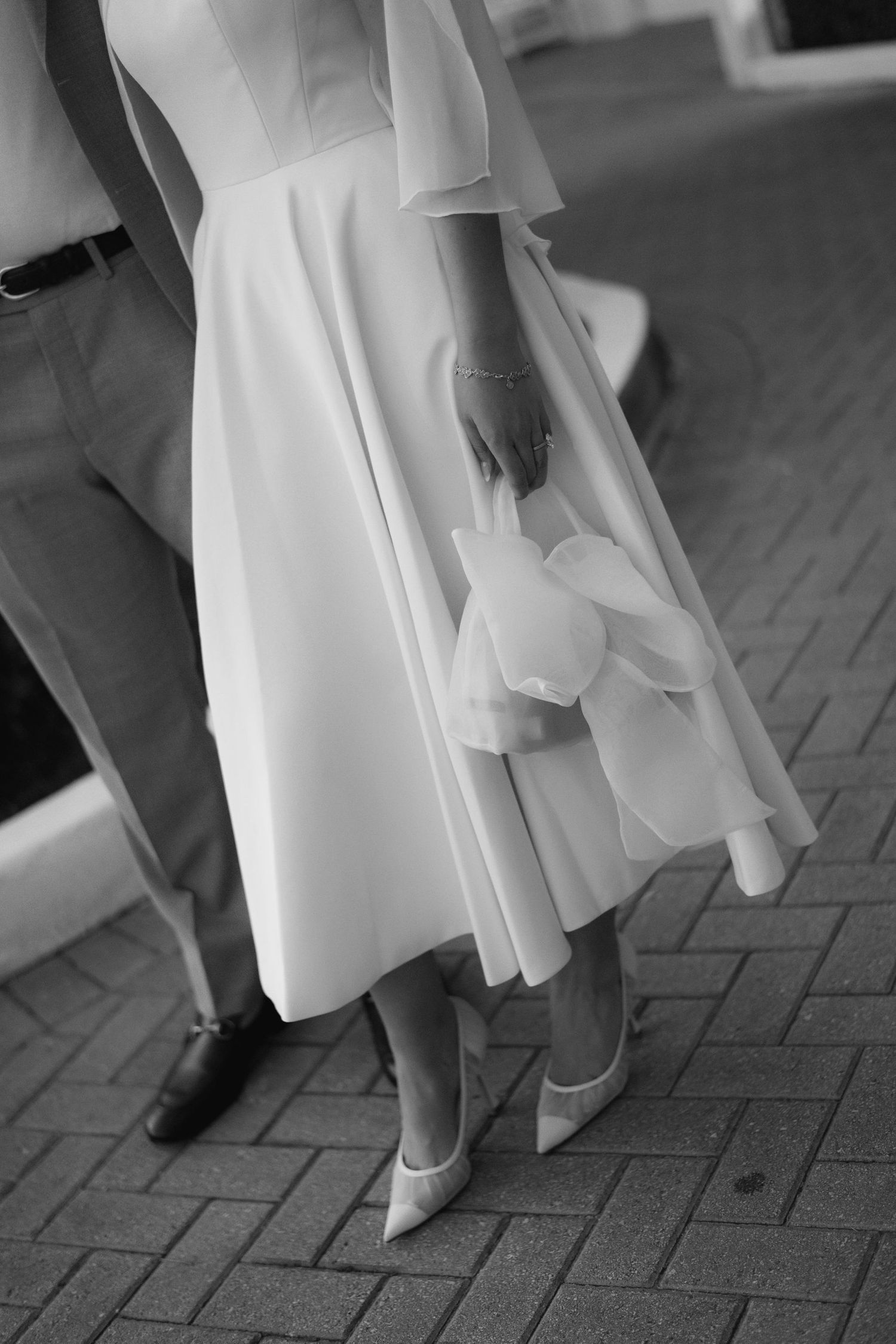 Black and white detail of formal attire and shoes on brick pavement.