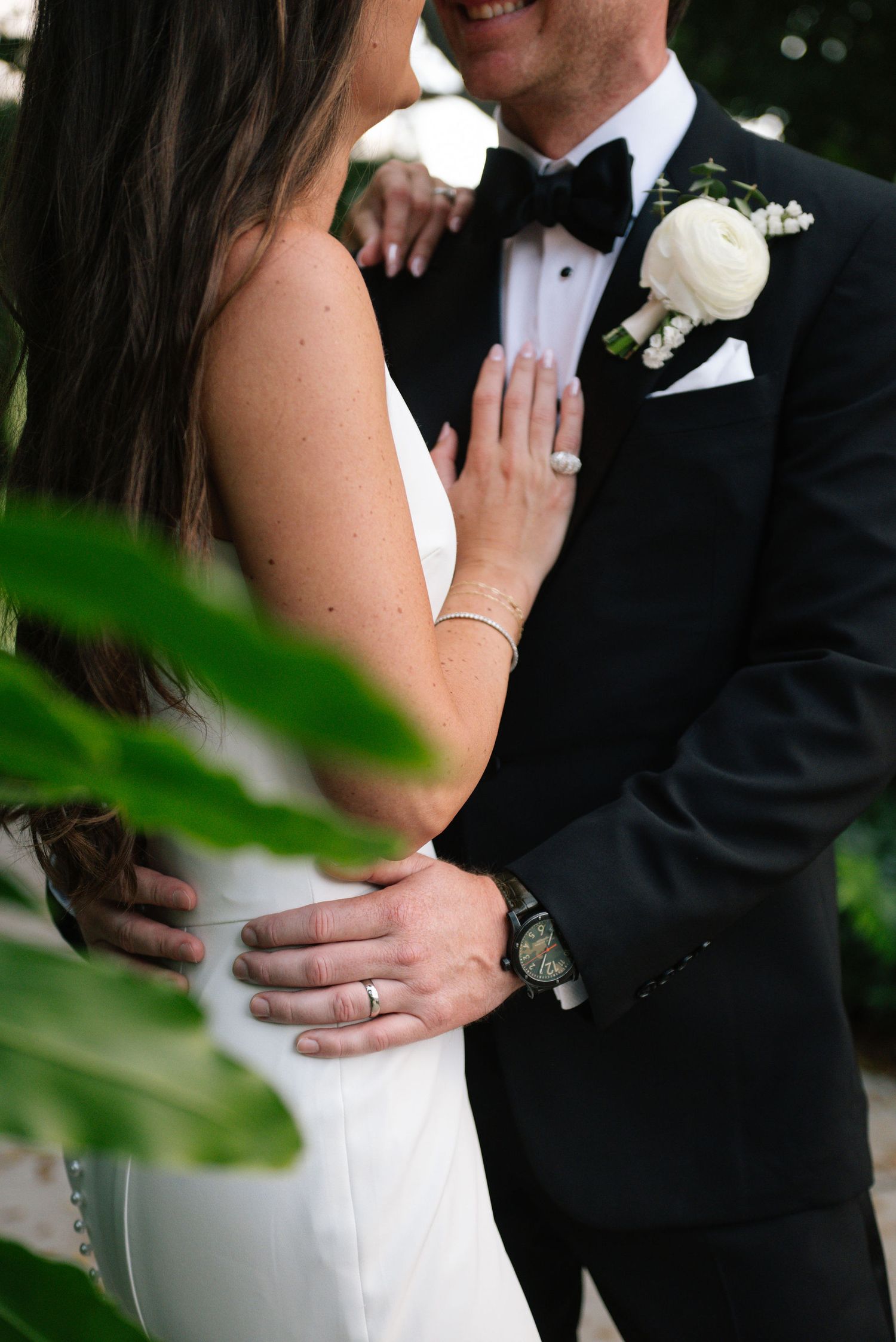 Close-up details of wedding couple embracing, showing formal attire and white boutonniere.