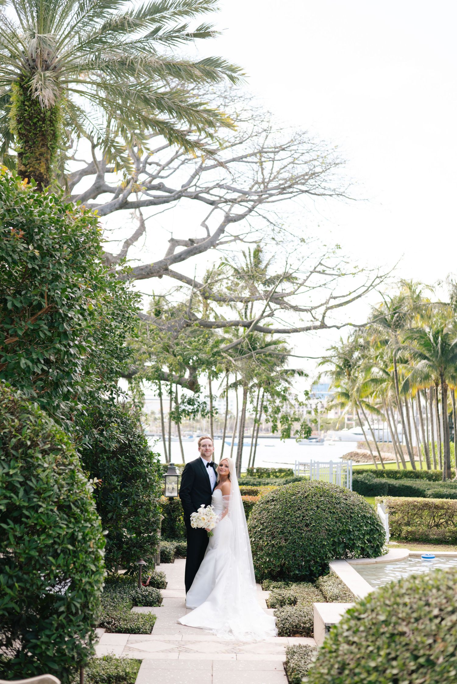 A wedding couple walks along a palm-lined pathway at a tropical resort venue during their photo session.