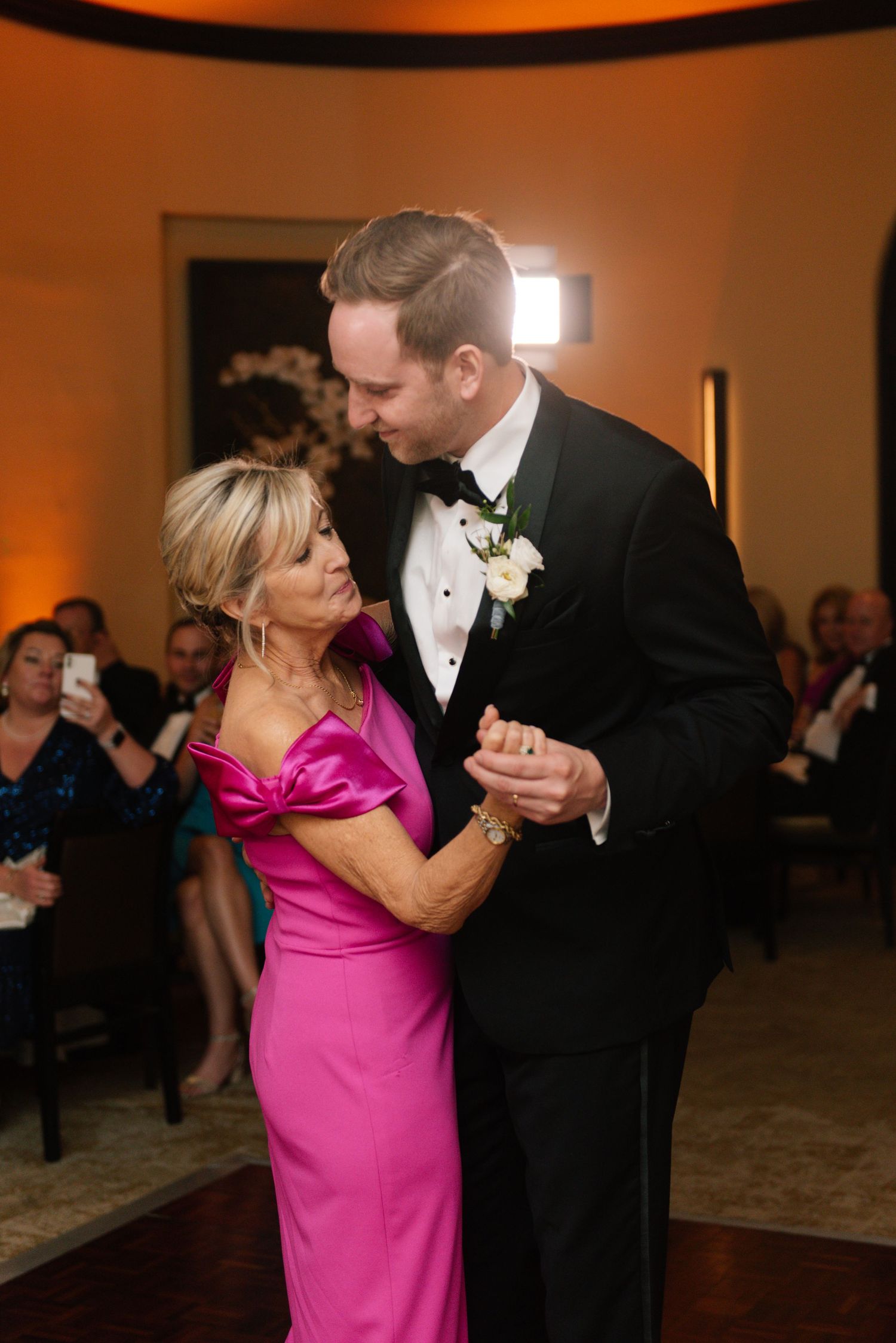 A touching dance moment at a formal event featuring a bright pink dress and black tuxedo.