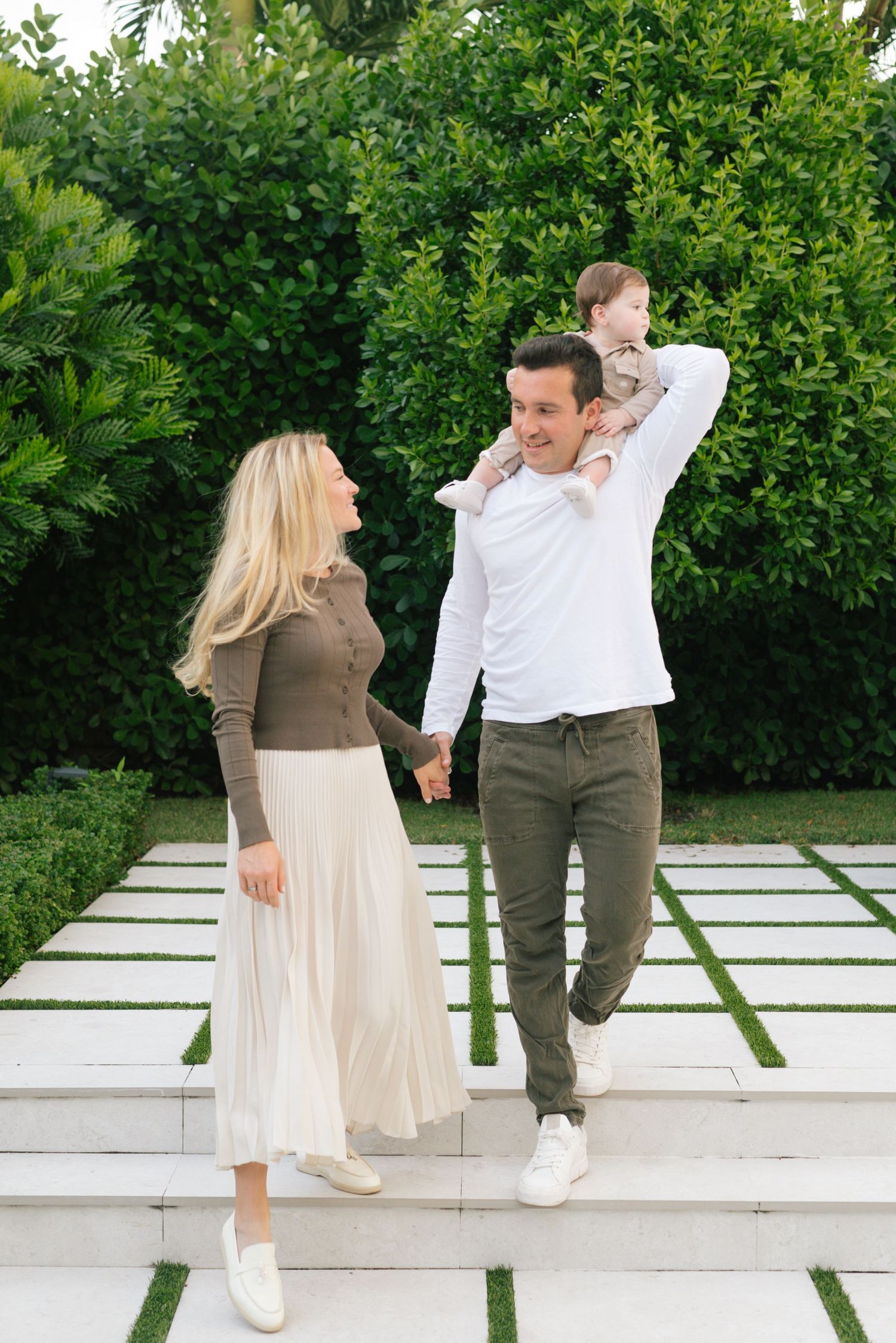 A joyful family moment on white stone steps with lush green hedges in the background.
