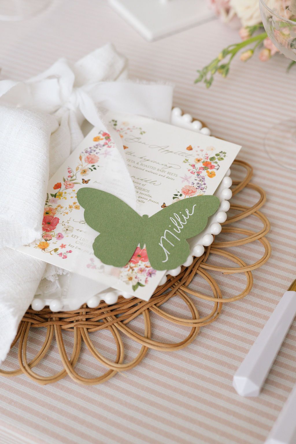 Delicate floral place card with green butterfly detail on decorative gold wire holder.