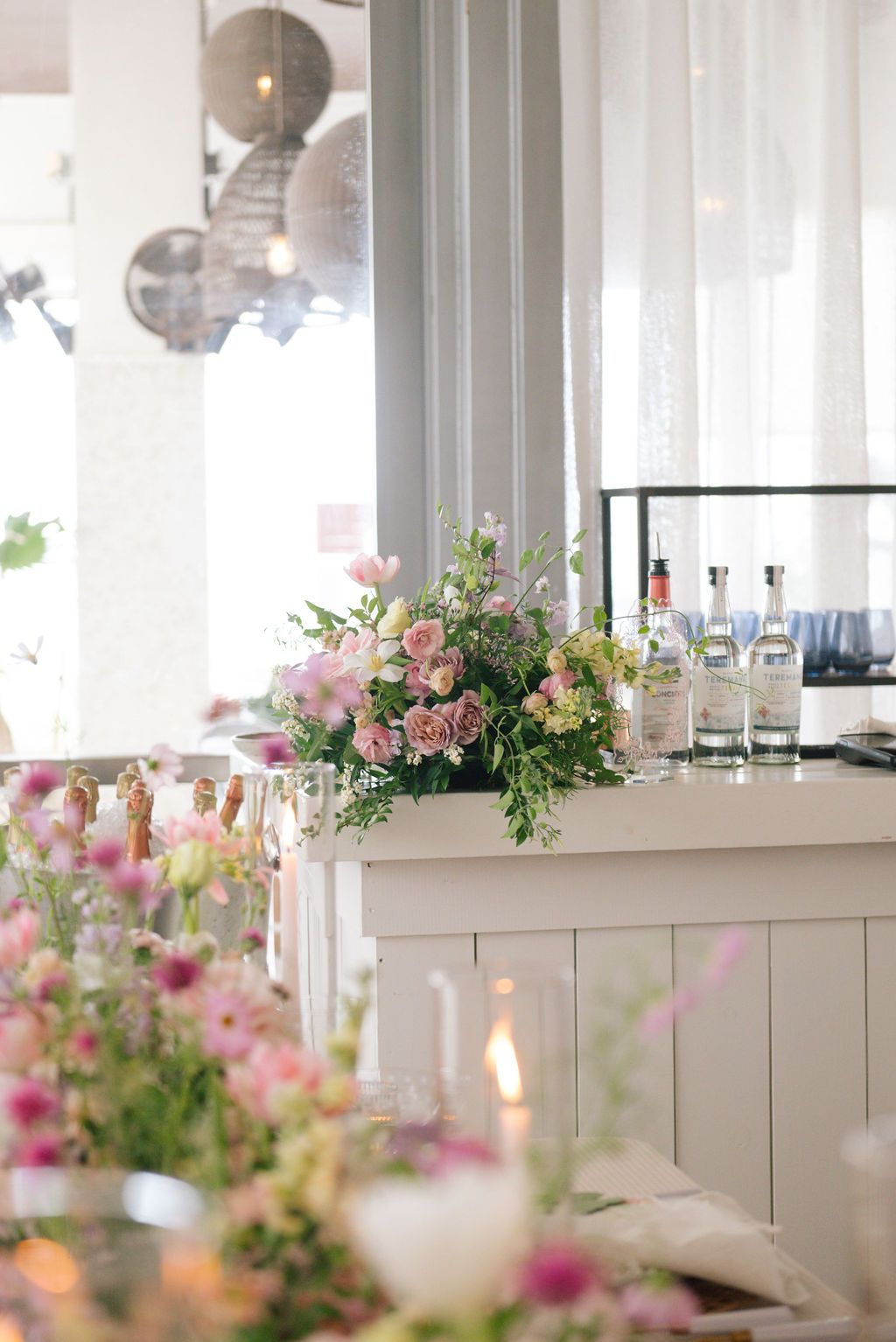 Elegant bar setup with pink floral arrangements and bottles displayed on white counter.