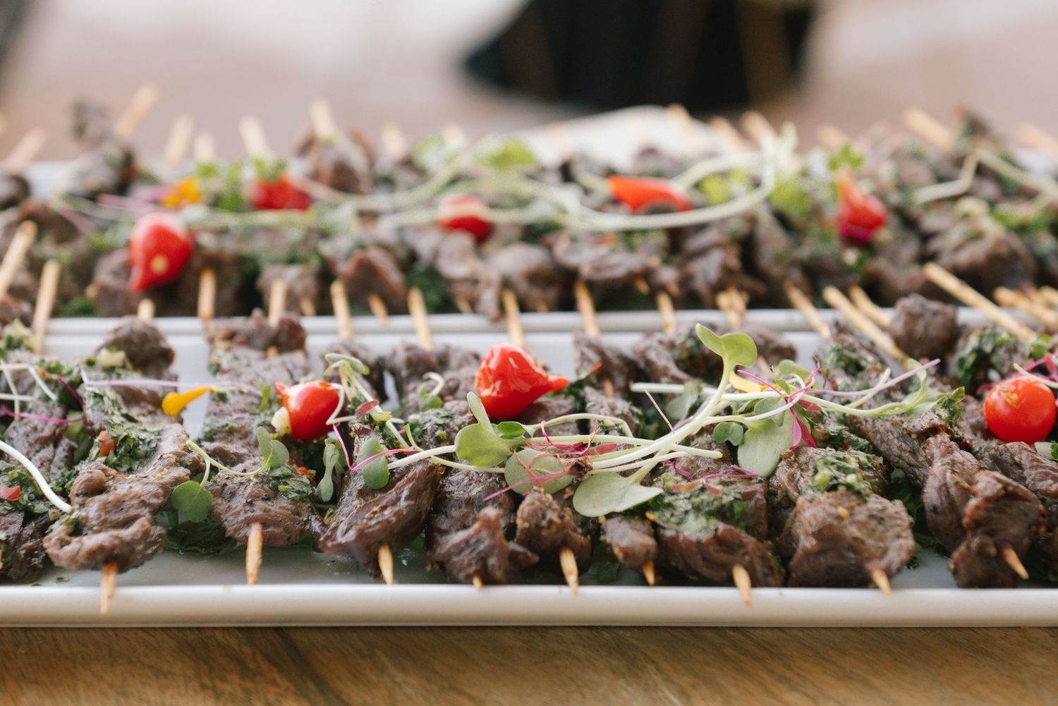 Appetizing skewered beef yakitori with green garnish and red cherry tomatoes arranged on a white serving platter.