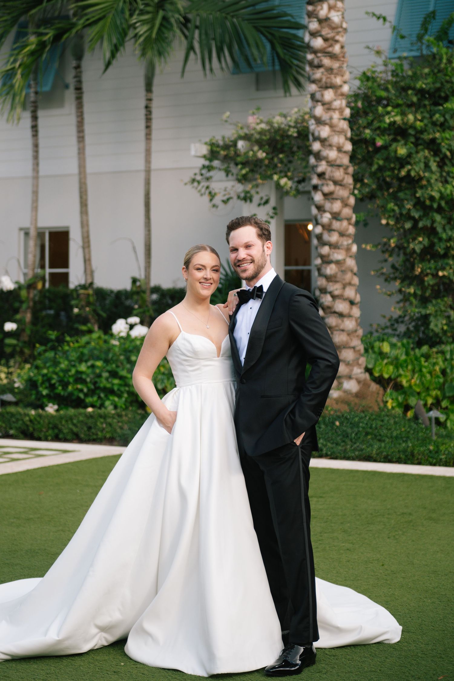 Bride and groom share intimate moments on manicured lawn with palm trees.