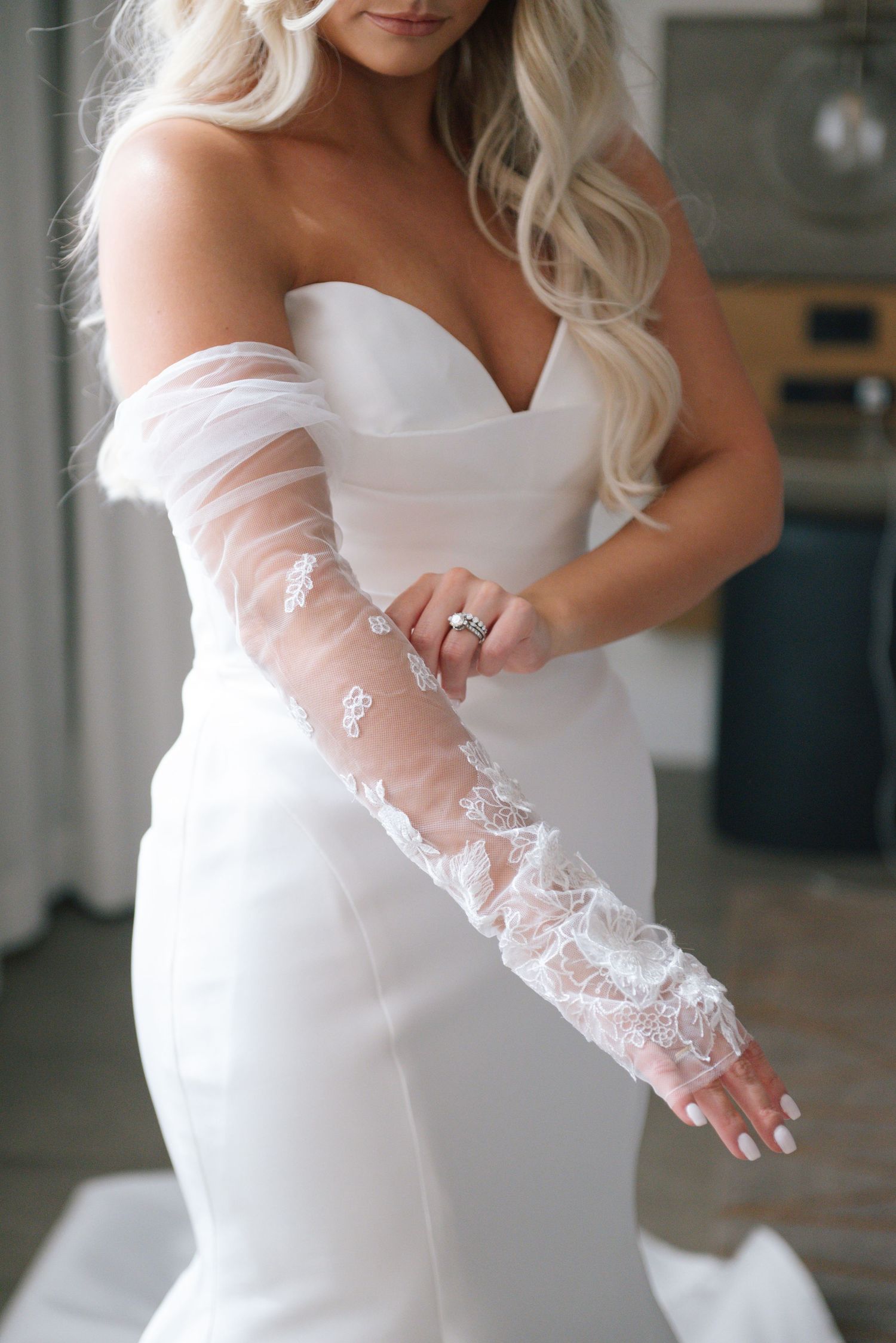 Close-up details of a white wedding dress with delicate sheer lace sleeves and elegant embellishments.