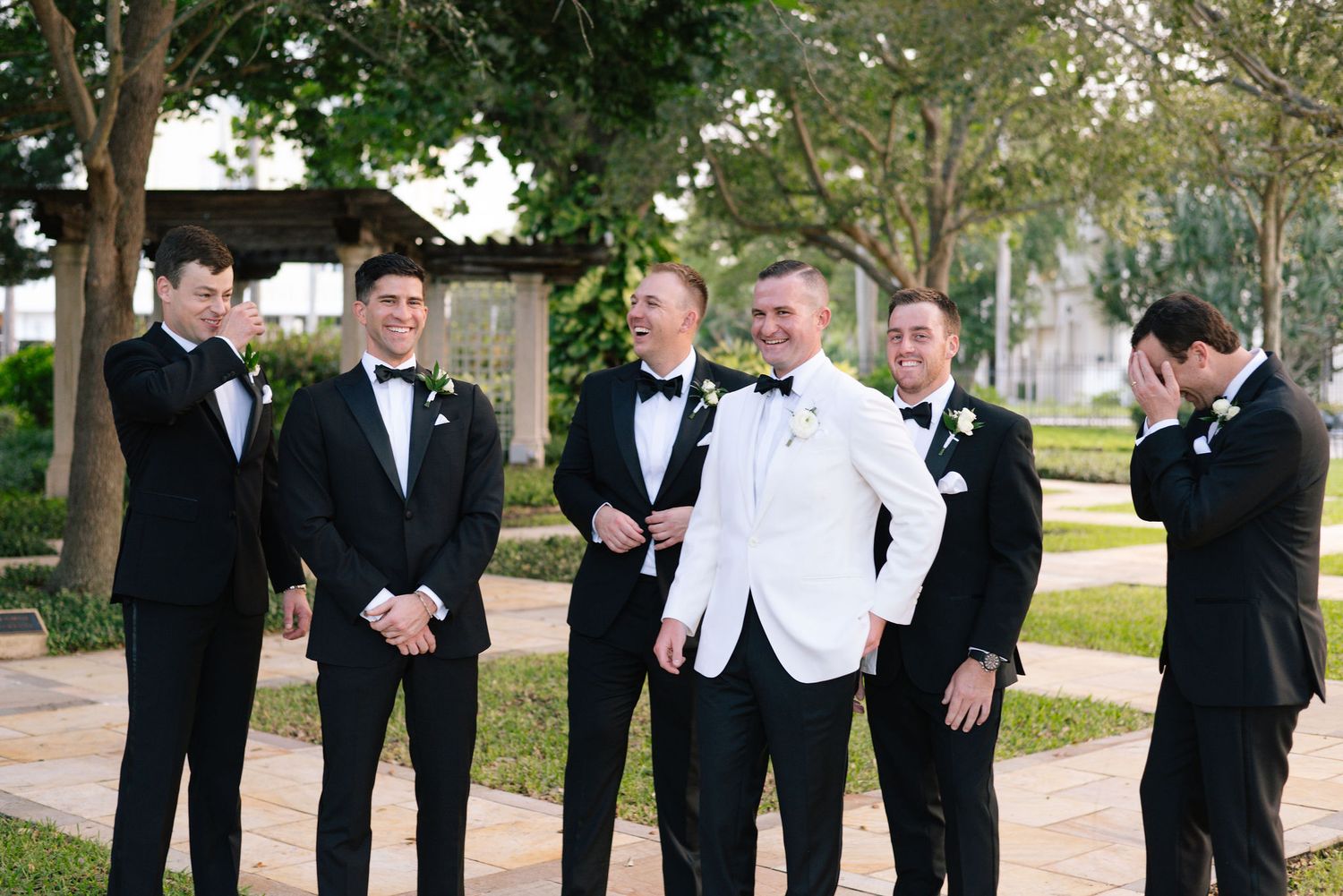 Groomsmen in formal attire share a candid moment outdoors during a wedding celebration.