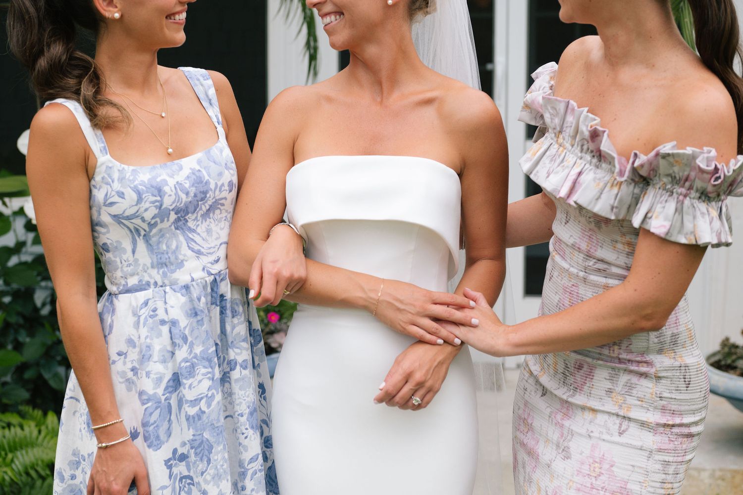 Wedding party members in floral and solid dresses share candid moment during outdoor celebration.