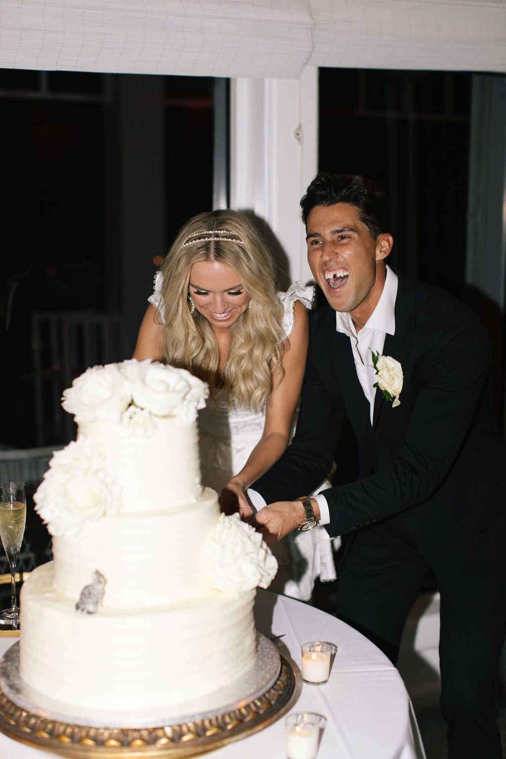 Newlyweds share a playful moment while cutting their white wedding cake together.