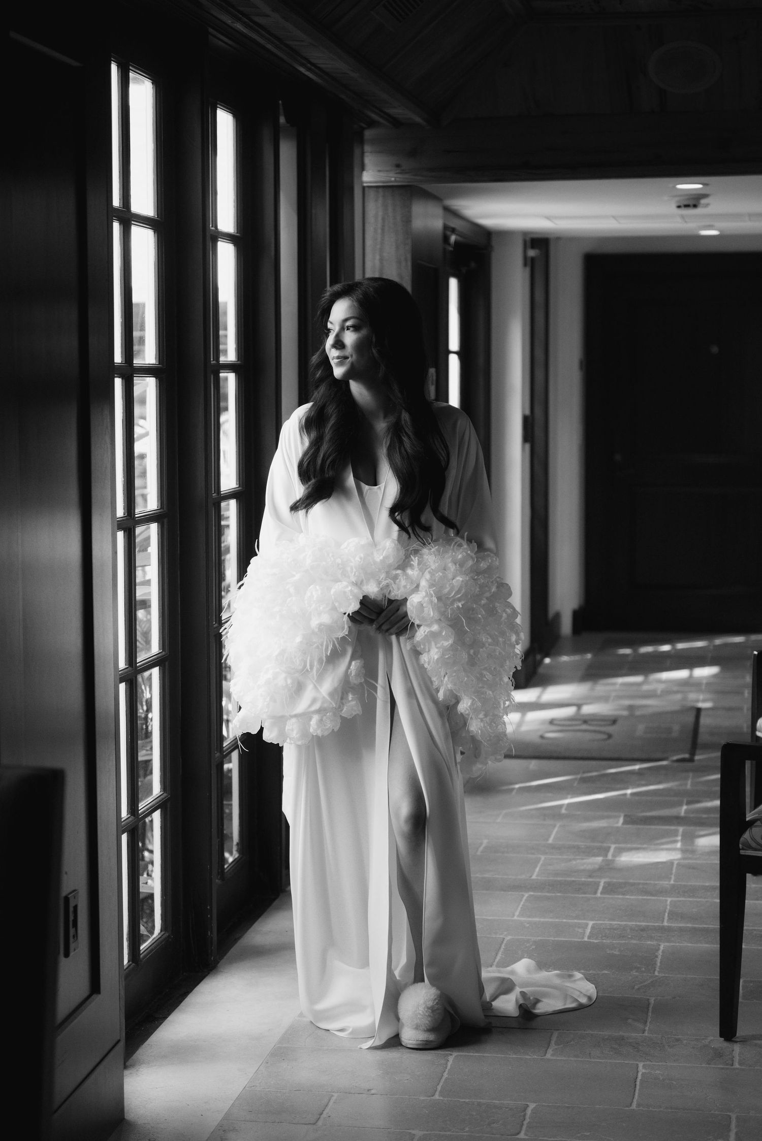 Dramatic black and white photo of someone in white walking down a modern hallway with large windows.