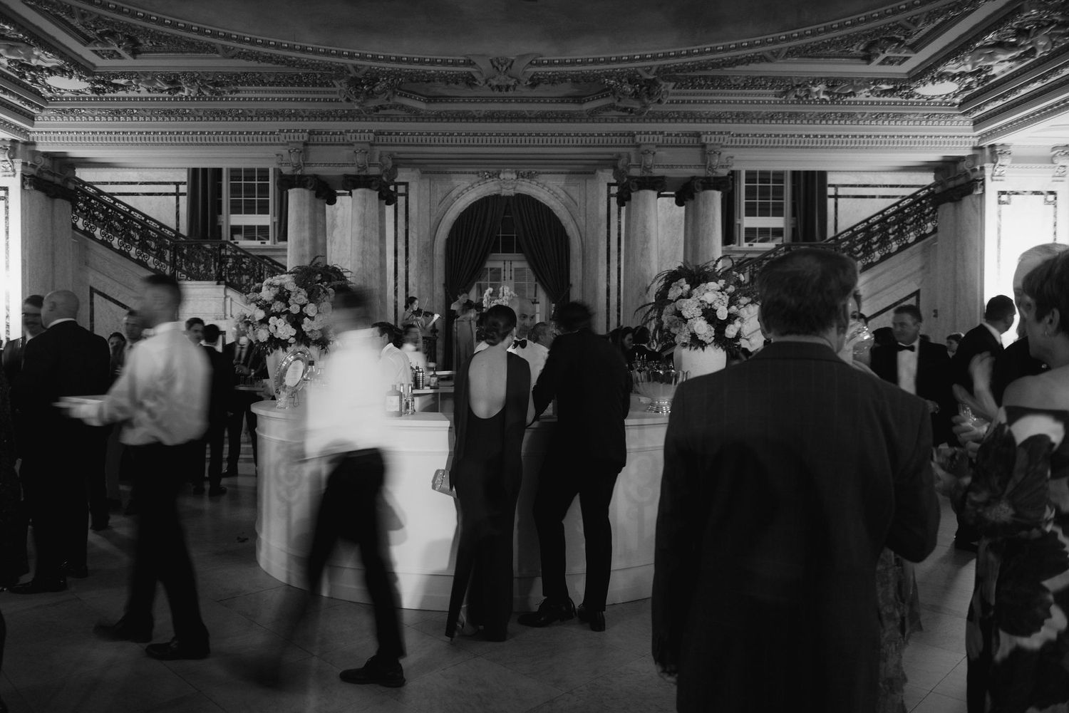 Black and white panoramic view of guests mingling at an elegant indoor event.