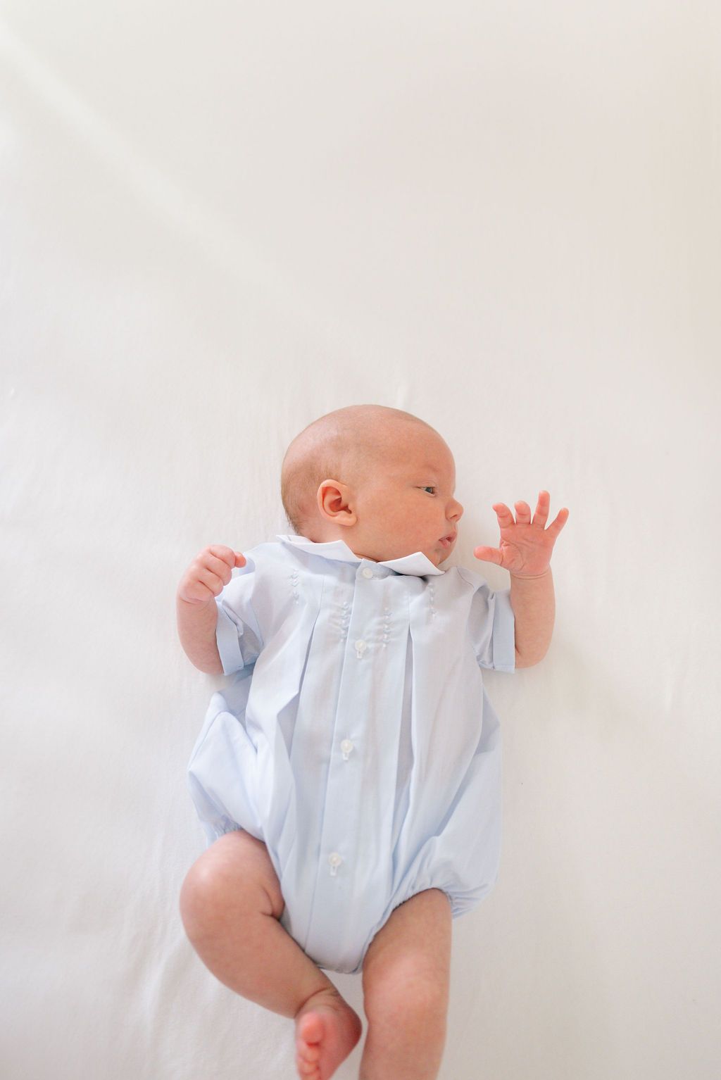 Newborn baby in light blue romper lying on white background with arms stretched.