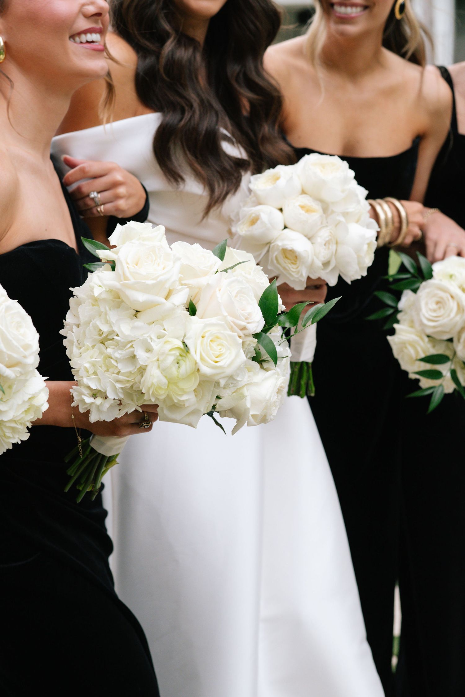 Wedding party members in black dresses holding elegant white rose bouquets.