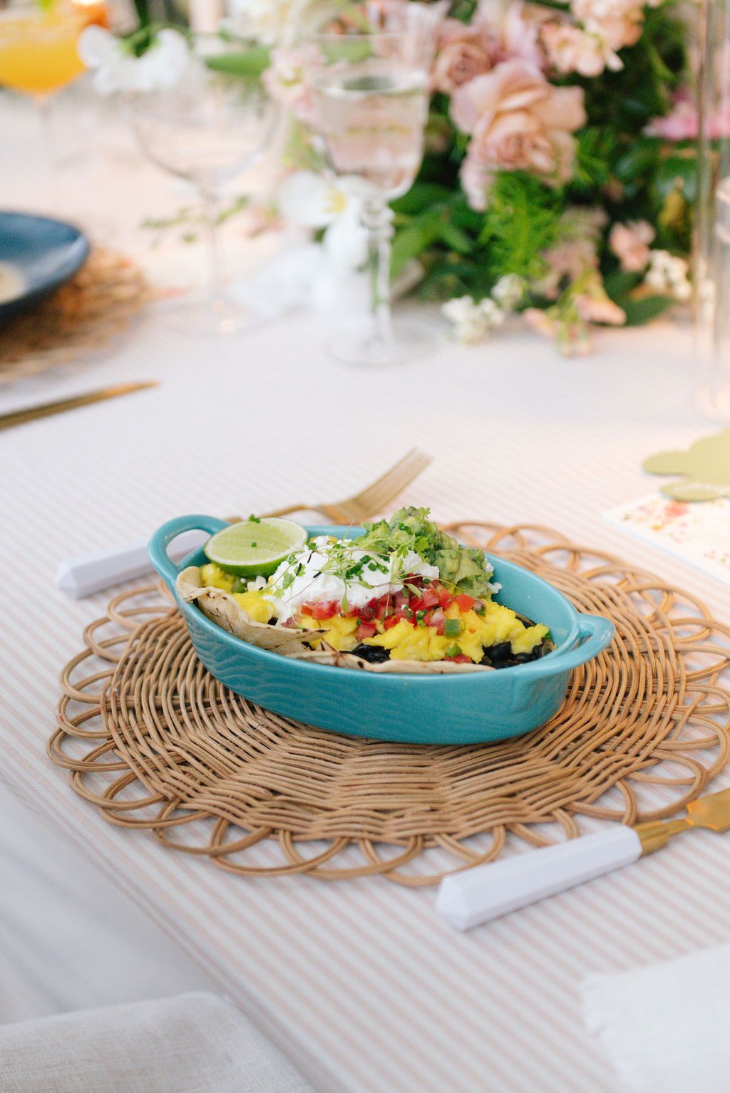Colorful dish served in turquoise ceramic bowl on woven placemat with floral centerpiece.
