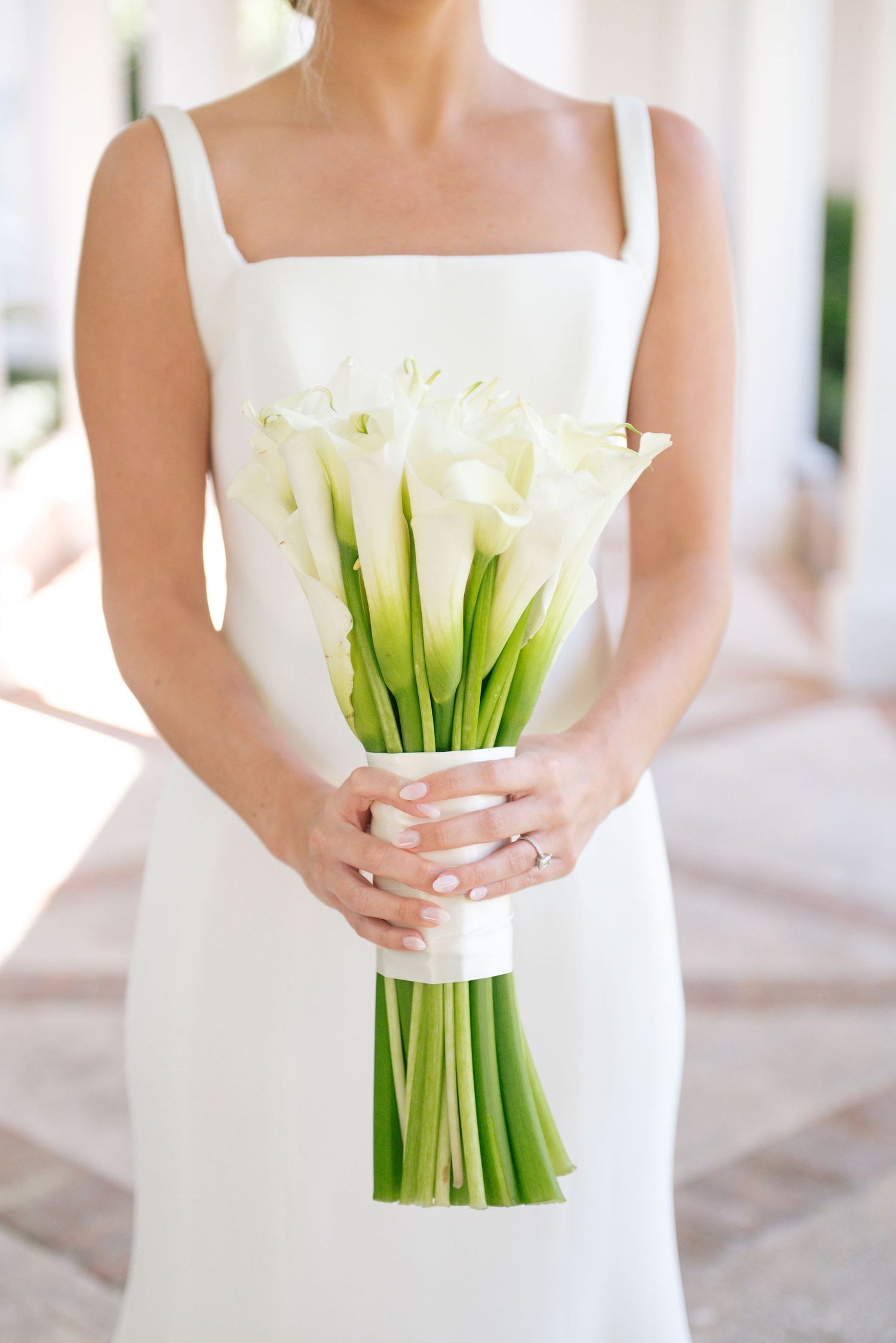 White calla lily bouquet held by hands in a simple white wedding dress.