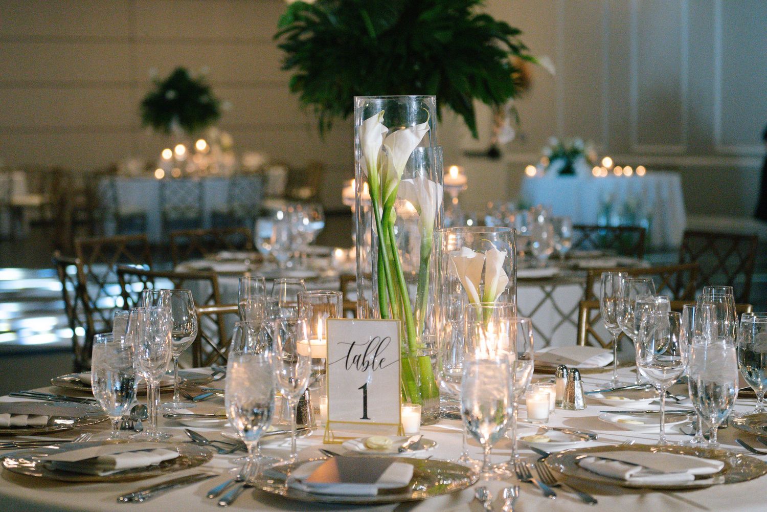 Elegant wedding reception tables set with fine china, crystal glassware and white floral centerpieces.