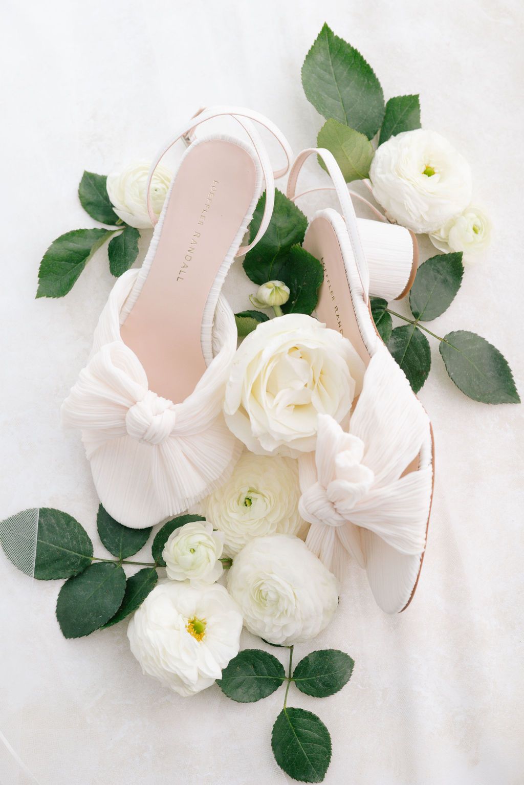 Delicate pink ballet shoes surrounded by fresh white roses and green leaves.