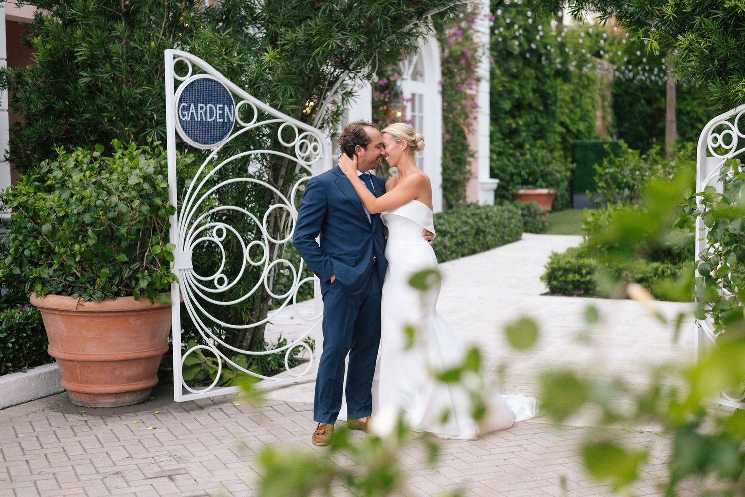 Wedding couple posing near decorative garden entrance with lush greenery.