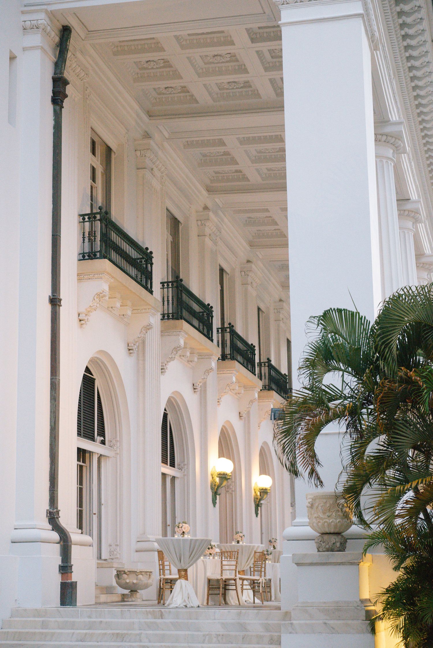 White colonnade walkway with green railings and palm trees at luxury venue.