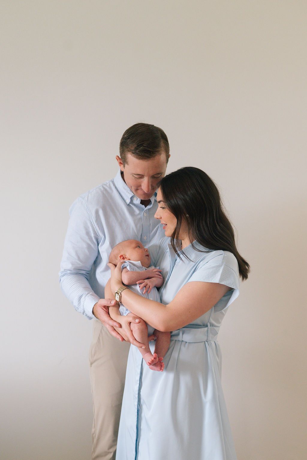 Parents in coordinating blue and white outfits tenderly holding their newborn baby.