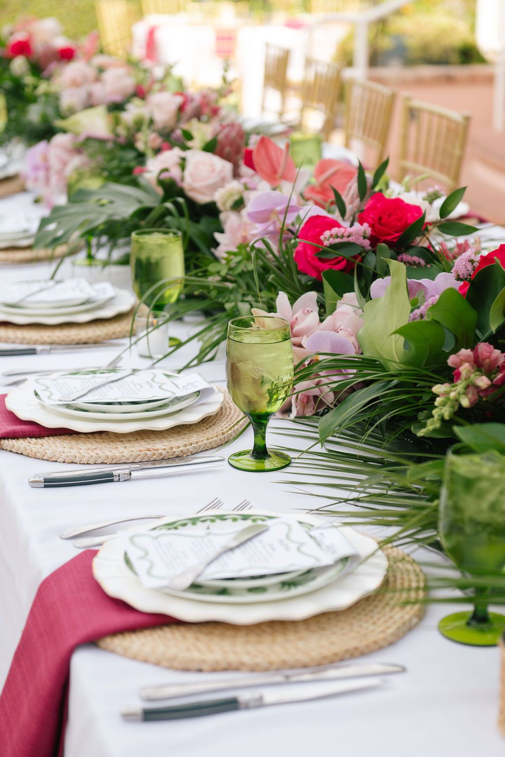 Elegant table setting with pink and white flowers, woven placemats, and green glassware for a wedding reception.