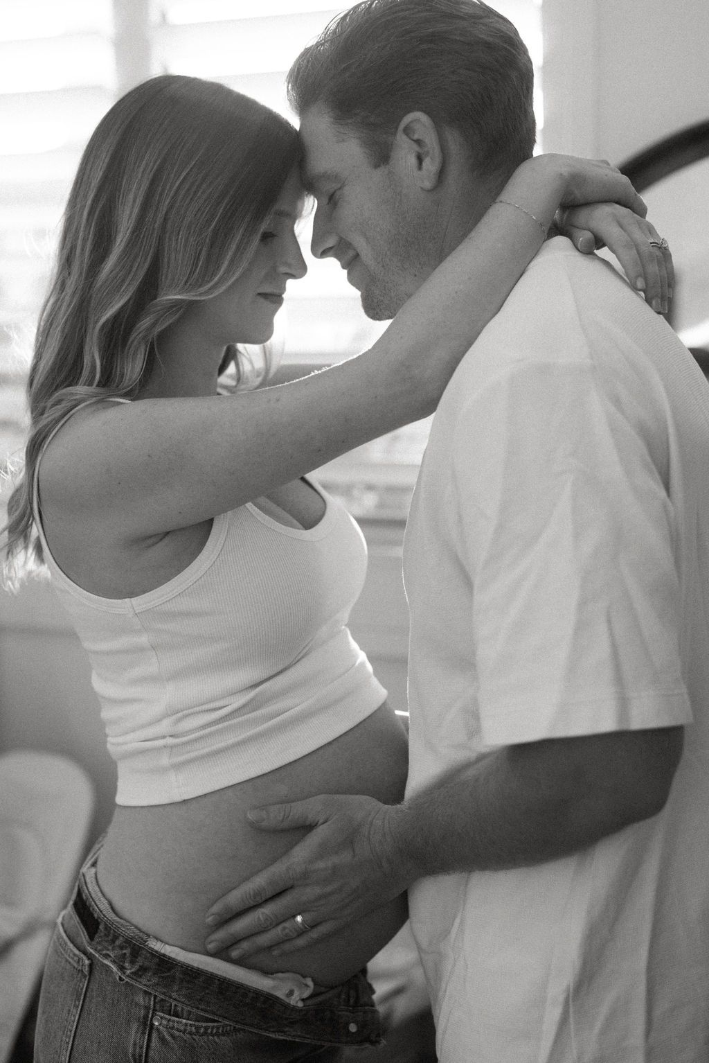 Couple in white tops and jeans sharing tender moments in a bright room.