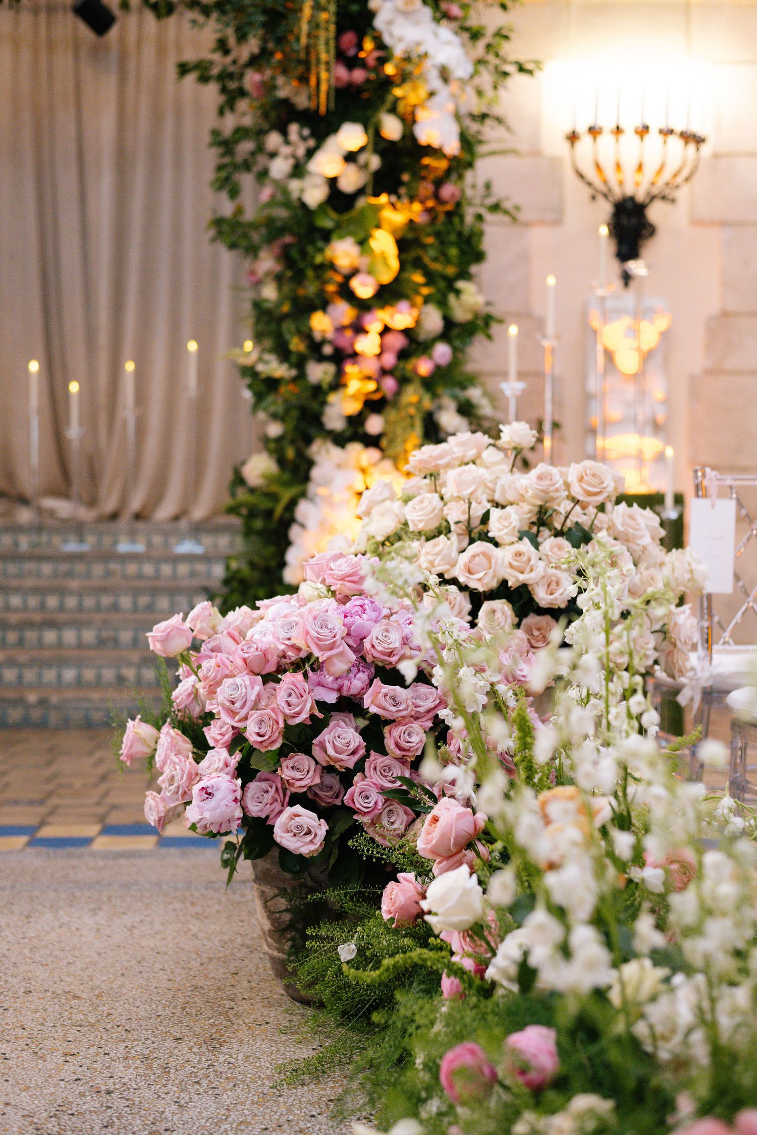 Elegant floral arrangements with pink roses and white flowers line a wedding ceremony aisle.