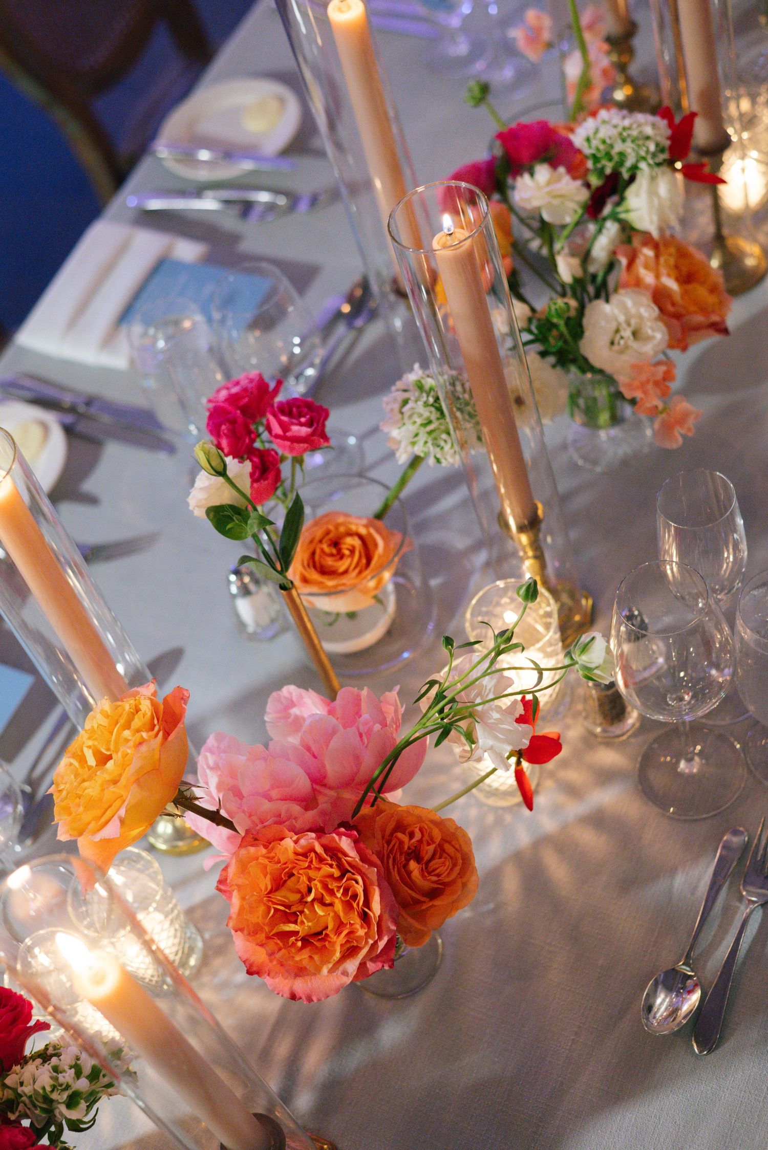 Elegant wedding table setting with pink and orange roses, candles, and glassware.