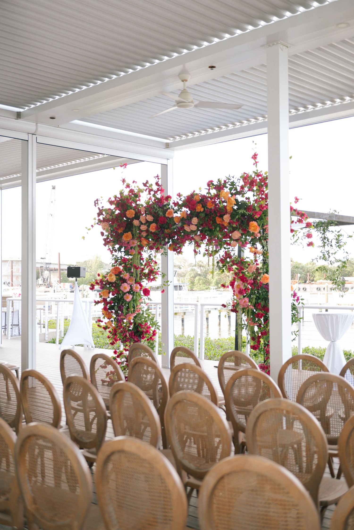 A covered outdoor event space with rows of tan chairs and floral arch decorations.