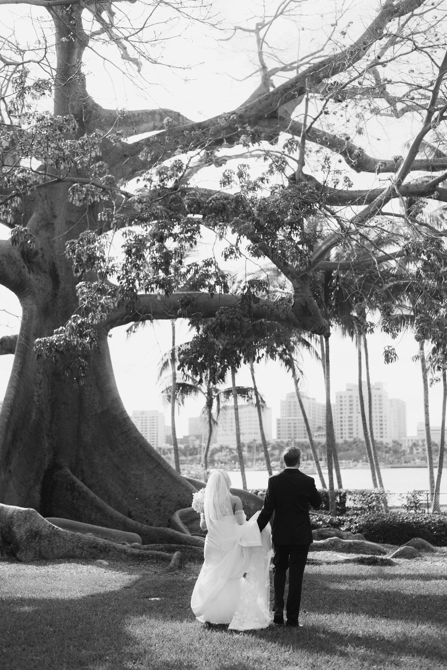 Black and white photo of a couple under a majestic oak tree by the water.