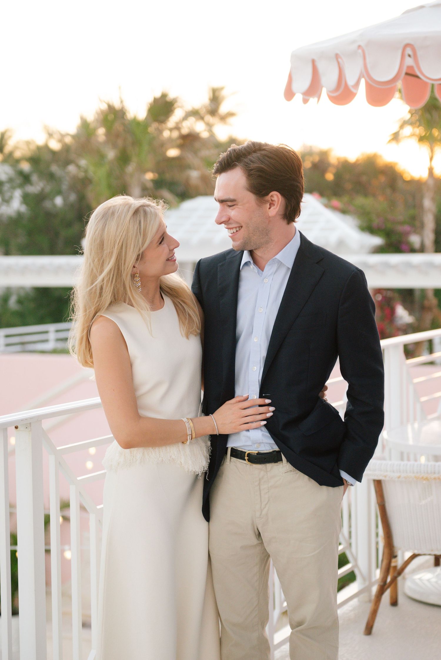 Couple sharing a romantic moment on a balcony at sunset under a striped umbrella.