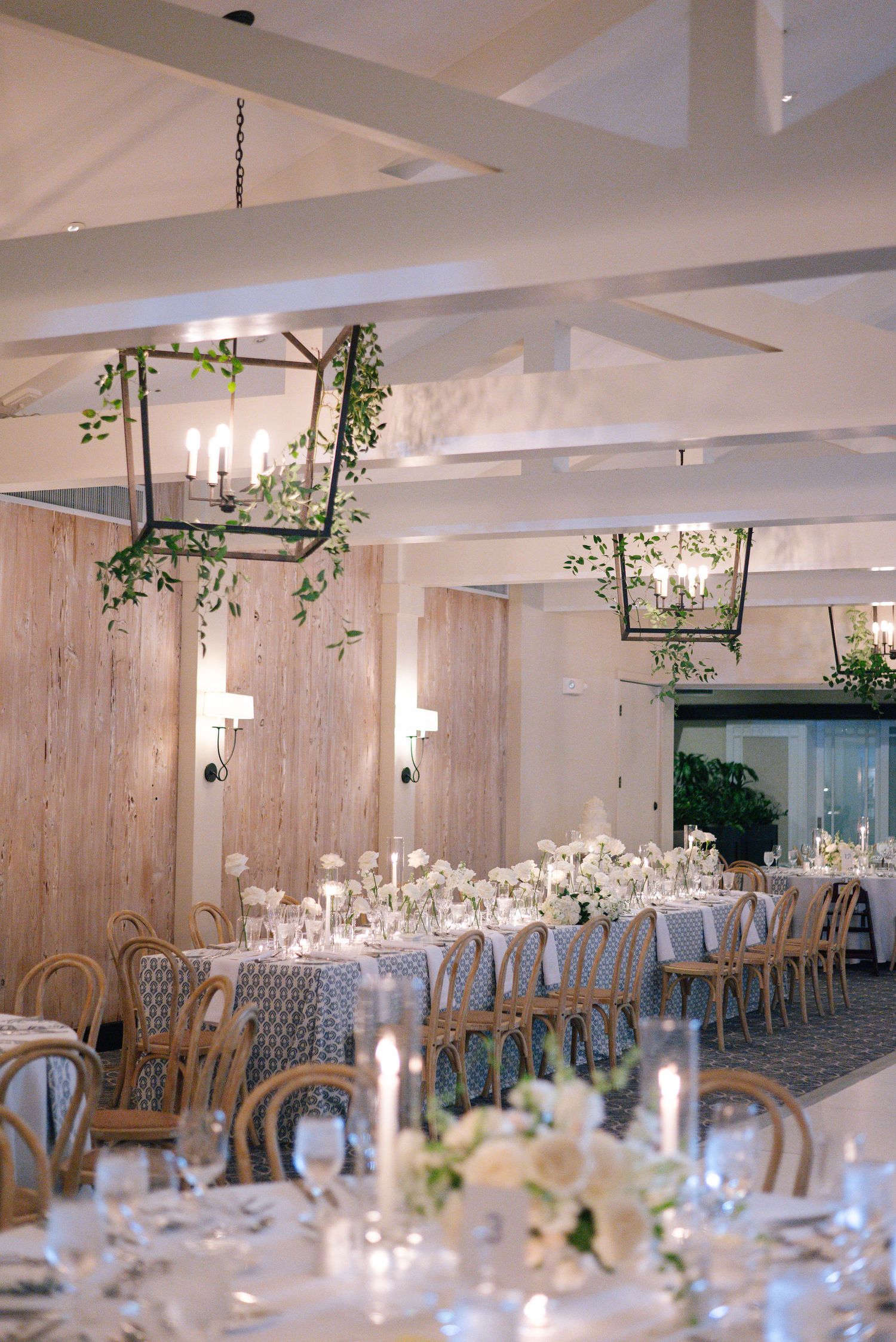 Elegant wedding reception venue with white floral centerpieces, candlelight and hanging greenery in a modern white space.