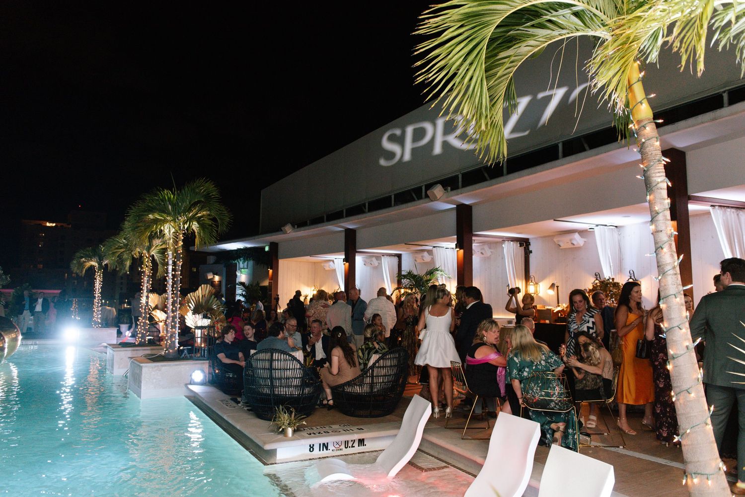 Nighttime pool party scene with palm trees and crowd at SPR venue.