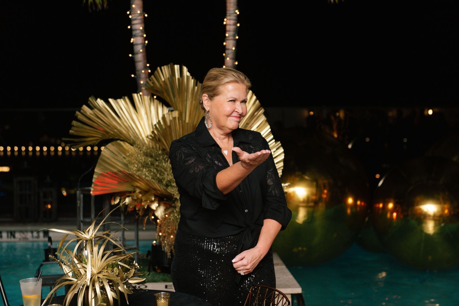 Event speaker in black attire presenting against a backdrop of illuminated palm trees.