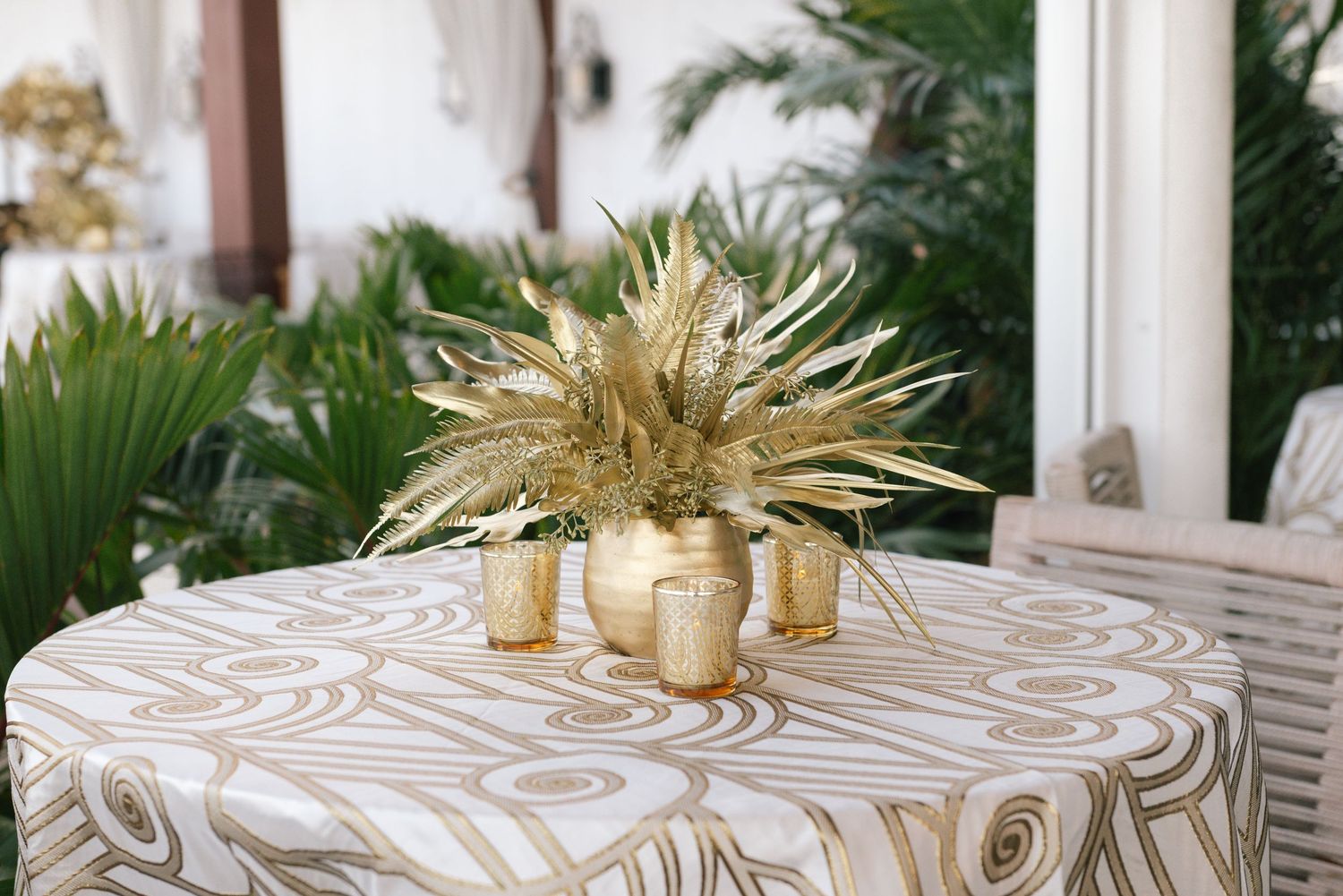 Wedding reception tables decorated with patterned linens and gold centerpieces in a bright indoor space.